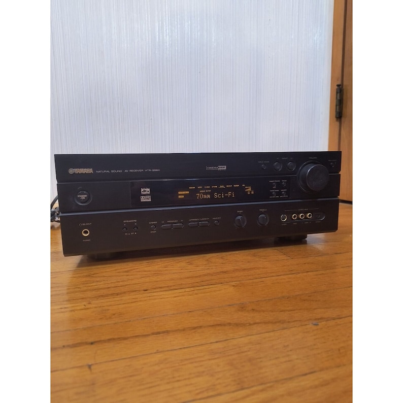 Puede incluir: Un receptor AV Yamaha Natural Sound negro con una pantalla digital que muestra "70mm Sci-Fi".