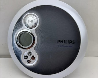 May include: A silver and gray Philips portable CD player. The device has a circular design with a digital display and control buttons. The text "PHILIPS" and "45 SECONDS ESP" are printed on the front.