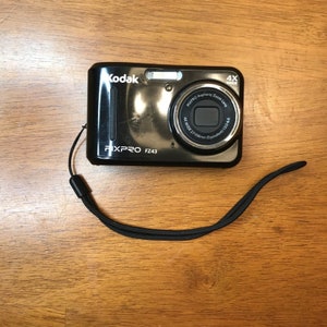 May include: A black Kodak EasyShare  FX PRO FZ43 digital camera with a black wrist strap. The camera has a 4x wide zoom lens and a silver lens ring.