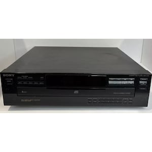 Może przedstawiać: Czarny odtwarzacz CD Sony na 5 płyt z wyświetlaczem cyfrowym i systemem wymiany płyt. Odtwarzacz ma wiele przycisków do sterowania odtwarzaniem i funkcjami.