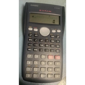 May include: A dark gray Casio fx-82MS scientific calculator featuring a digital display showing a zero, a circular navigation button, and a numeric keypad with various mathematical function keys labeled in white, red, and yellow text.