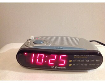 May include: A silver and black digital clock radio with a red LED display showing the time 10:25. The clock radio has a sleep off button and AM/FM radio tuning knobs. The clock radio also has a battery backup feature and displays the frequency range for AM and FM radio.