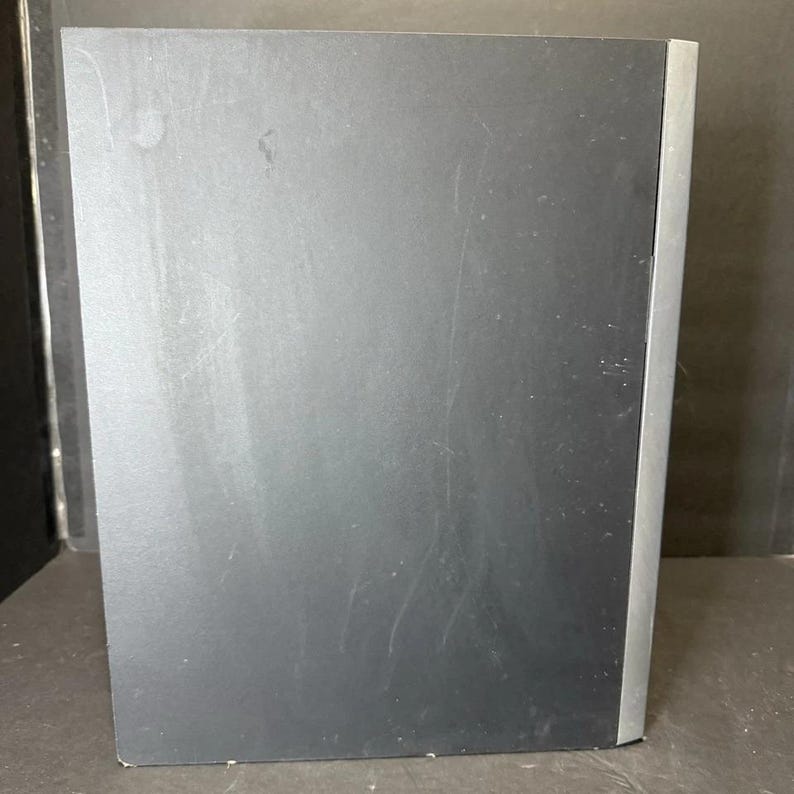 May include: A rectangular black object with a silver edge. The object has a smooth, matte finish and appears to be made of metal or a similar material. The surface has minor scratches. The item is likely a component of a larger electronic device.