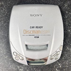 May include: Silver Sony Discman ESP2 portable CD player. The device has a curved design with buttons for volume, menu, and playback. The text "CAR READY" and "Discman ESP2" are visible on the device.