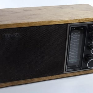 May include: A vintage wooden Sony AM/FM radio with a black speaker grille and silver faceplate. The radio has knobs for volume, tuning, and tone control.