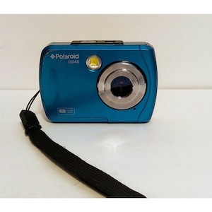 May include: A blue Polaroid ISO48 digital camera with a black wrist strap. The camera has a silver lens and a small yellow flash.