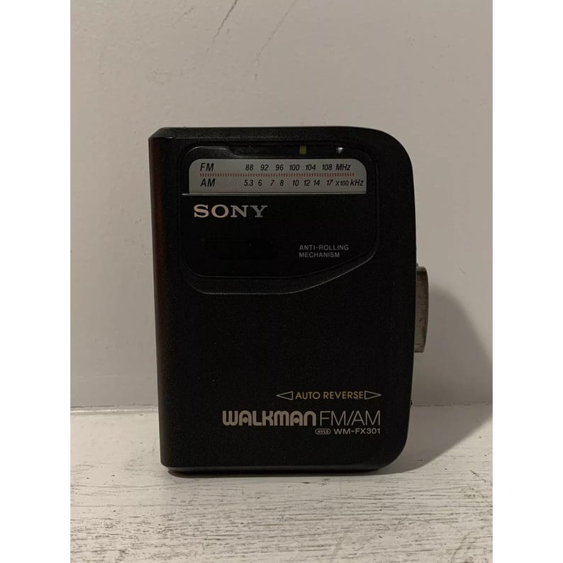 May include: A black Sony Walkman FM/AM radio cassette player with the model number WM-FX301. The radio has a digital tuner with frequency markings for FM and AM bands. The radio has an anti-rolling mechanism and an auto reverse feature.