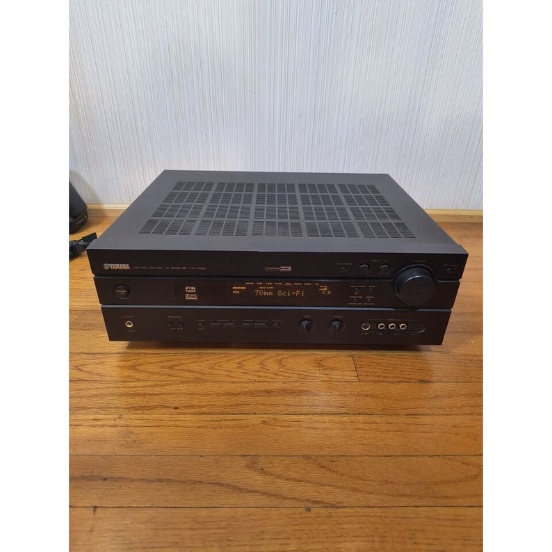 Puede incluir: Un receptor Yamaha 70Wx7 negro con una placa frontal plateada y una pantalla digital. El receptor tiene una variedad de botones y perillas, incluyendo una perilla de volumen, un bot&oacute;n de encendido y un selector de fuente. El receptor est&aacute; sentado sobre una superficie de madera.