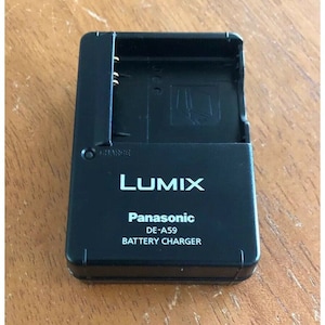 May include: Black Panasonic Lumix DE-A59 battery charger for cameras. The charger has a slot for the battery and a charging indicator light.