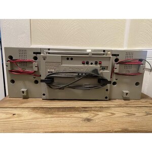 May include: A beige stereo system with a cassette player, radio tuner, and CD player. The stereo has a caution label and a red and black wire attached to the back.