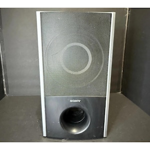 May include: A black Sony subwoofer speaker with a silver frame. The speaker has a mesh front with a large circular design in the center. The bottom section is solid black with a circular port. The Sony logo is visible.