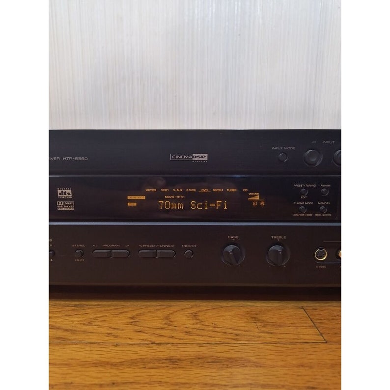 Puede incluir: Un receptor de cine en casa negro con una pantalla digital que muestra "70mm Sci-Fi". El receptor tiene varios botones y perillas, que incluyen volumen, graves, agudos y modo de entrada.