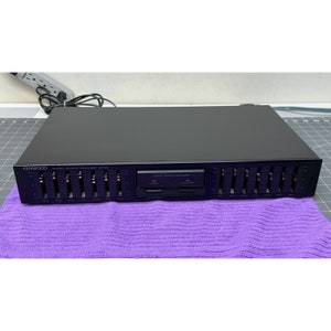 Puede incluir: Un ecualizador gráfico estéreo Kenwood negro con 10 deslizadores. El ecualizador tiene el texto "STEREO GRAPHIC EQUALIZER QE-201" impreso en la parte delantera.