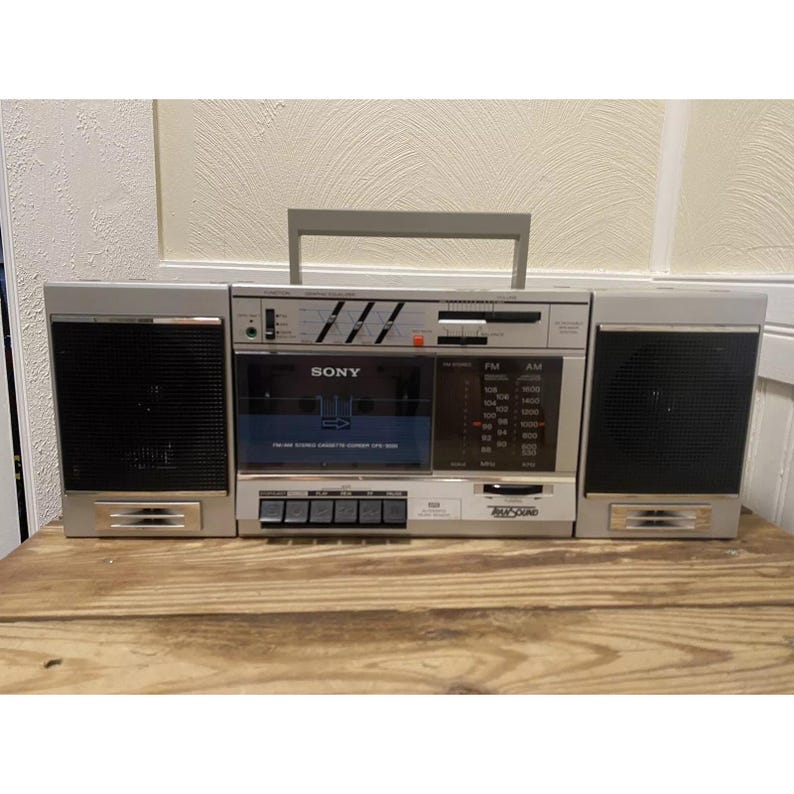 May include: A silver Sony boombox with a cassette player, AM/FM radio, and two speakers. The boombox has a black cassette tape slot and a black display screen with the word "SONY" printed on it.