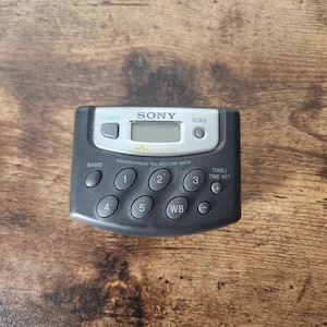 Peut inclure: Un radio-réveil Sony Weather/FM/AM Walkman noir avec un cadran argenté et un écran numérique. Le radio-réveil possède un certain nombre de boutons, notamment l'alimentation, l'horloge, la bande, l'accord/la mise à l'heure et WB.
