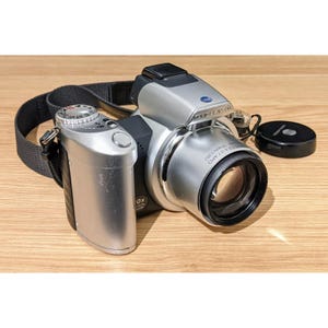 May include: A silver digital camera with a black lens and a black strap. The camera has a zoom lens with the text "3.5-35.0mm 1:3.5-5.6" printed on the lens. The camera also has a zoom control on the side with the text "10X OPTICAL ZOOM".