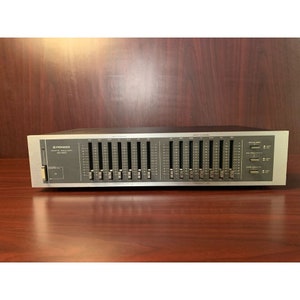 Könnte beinhalten: Ein silberner Pioneer Graphic Equalizer SG-9500 mit 10 Schiebereglern. Der Equalizer hat eine schwarze Frontplatte mit weißem Text und Markierungen.