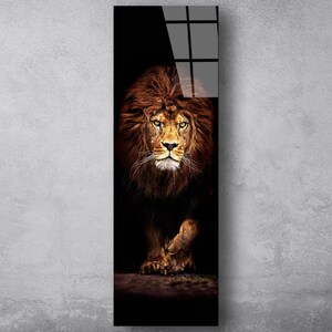 May include: A vertical art print featuring a majestic lion. The lion's face and mane are a rich brown, with piercing yellow eyes. The background is dark, emphasizing the lion's powerful presence. The artwork is mounted on a glossy black surface.