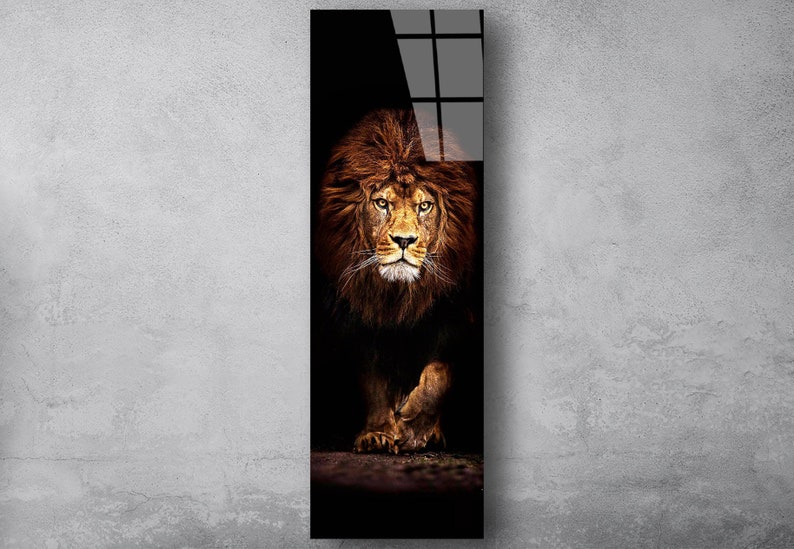 May include: A vertical art print featuring a majestic lion. The lion's face and mane are a rich brown, with piercing yellow eyes. The background is dark, emphasizing the lion's powerful presence. The artwork is mounted on a glossy black surface.