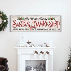 May include: A white wooden sign with red and green accents reads "The Wilson Family Santa's Workshop Limited Edition Toys Handcrafted at the North Pole". The sign is hanging above a white fireplace with stockings hanging from the mantle.