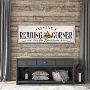 May include: A white wooden sign with the text "Jasmine's Reading Corner" and the words "Just One More Chapter" in a decorative font. The sign features a vintage illustration of a stack of books.