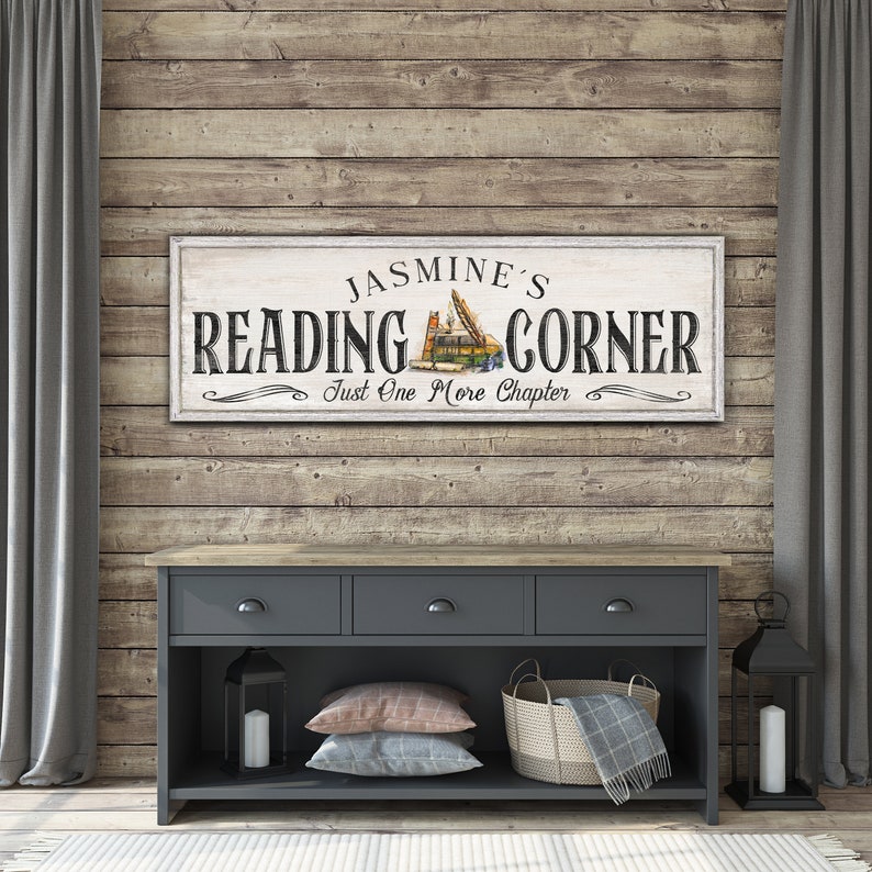 May include: A white wooden sign with the text "Jasmine's Reading Corner" and the words "Just One More Chapter" in a decorative font. The sign features a vintage illustration of a stack of books.