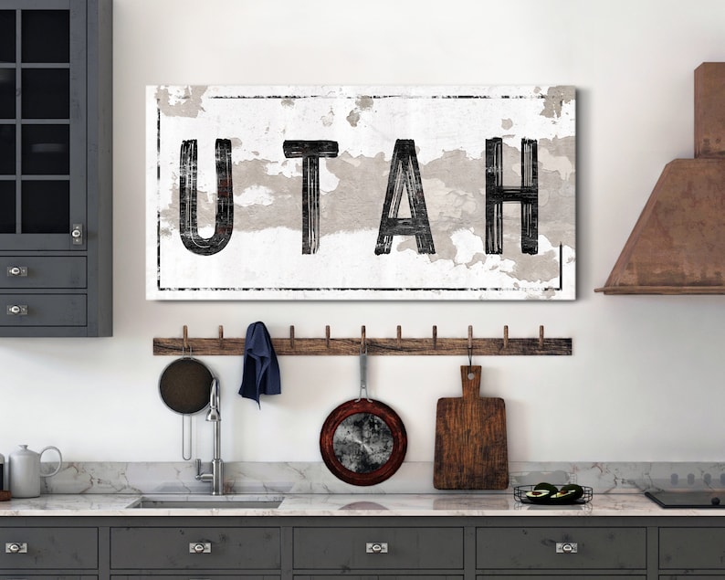 May include: A white canvas wall art print with black text that reads "UTAH" in a distressed font. The print is framed with a black border and has a white background with a distressed texture.