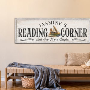 May include: White wooden sign with black text that reads "Jasmine's Reading Corner Just One More Chapter". The sign features a stack of books with a bookmark.