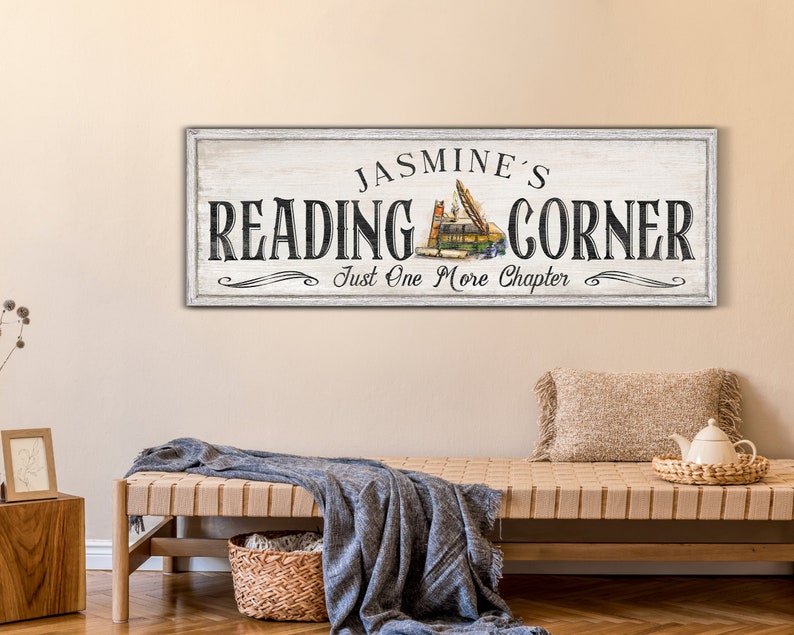 May include: White wooden sign with black text that reads "Jasmine's Reading Corner Just One More Chapter". The sign features a stack of books with a bookmark.