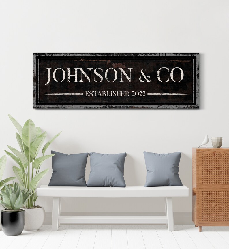 May include: A black and white sign with distressed edges and a rustic woodgrain texture. The sign reads "JOHNSON & CO ESTABLISHED 2022".