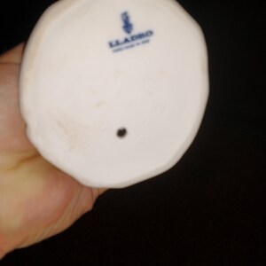 May include: The bottom of a white porcelain figurine with a blue and white Lladro logo.