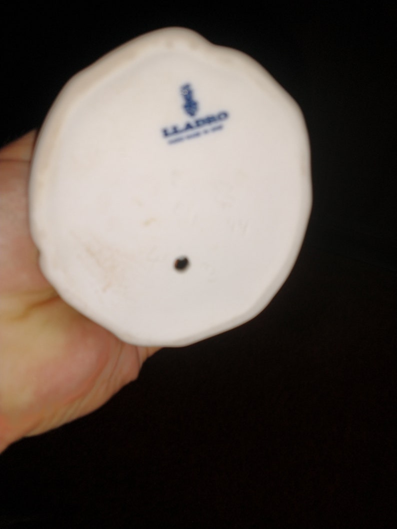May include: The bottom of a white porcelain figurine with a blue and white Lladro logo.