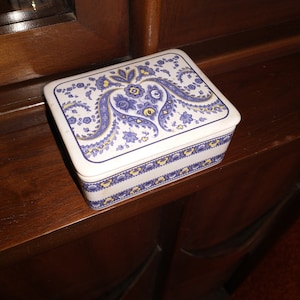 May include: A white rectangular box with a blue and yellow paisley design. The box has a heart shape in the center of the design.