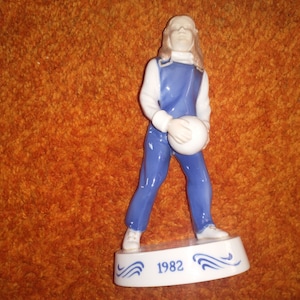 May include: A blue and white porcelain figurine of a person holding a white ball. The figurine is standing on a base with the year 1982 written on it.