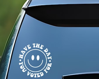 May include: White vinyl car sticker with a smiley face and the text "Have the day you voted for."