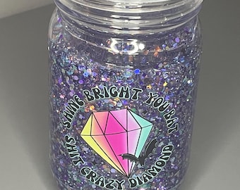 May include: A clear plastic tumbler with a purple glitter base and a black and white sticker that says "Shine Bright You Bat Shit Crazy Diamond" with a rainbow diamond and a bat graphic.