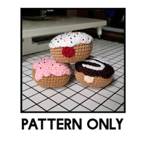 May include: Three crocheted donuts in a stack. The top donut has white frosting with colorful sprinkles and a red cherry. The middle donut has pink frosting and sprinkles. The bottom donut has chocolate frosting and a cream-colored swirl. The text "PATTERN ONLY" is at the bottom.