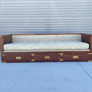 May include: A wooden sofa with a light beige fabric cushion and three drawers with brass hardware.