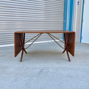 May include: A brown wooden extendable dining table with brass accents and a rectangular top. The table is folded and has a simple design.
