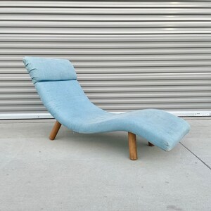May include: A light blue chaise lounge with a curved design and wooden legs. The lounge is made of fabric and has a comfortable, relaxed look.