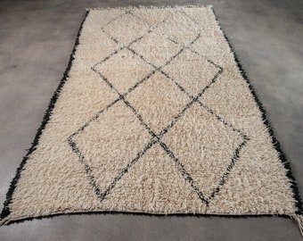 May include: A white shag rug with a black diamond pattern. The rug has a fringe border.