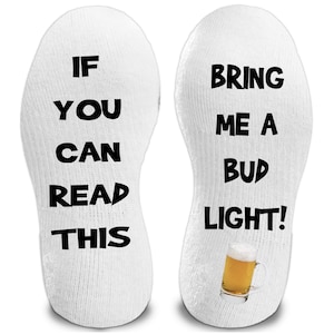May include: White socks with black text that reads "IF YOU CAN READ THIS" on one sock and "BRING ME A BUD LIGHT!" on the other. A small graphic of a beer mug is on the second sock.