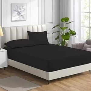 May include: A bed featuring a solid black fitted sheet and two matching black pillowcases. The bed is positioned against a white paneled headboard. The bedding set provides a uniform dark appearance against the light-colored bedroom furniture.
