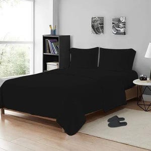 Op de afbeelding: Een effen zwarte beddengoedset bestaande uit een laken, een hoeslaken en twee bijpassende kussenslopen. Het beddengoed ligt op een bedframe en heeft een gladde, gelijkmatige textuur en een diepe, donkere kleur die het matras volledig bedekt.