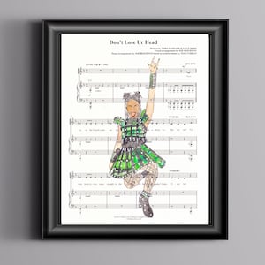 Può includere: Una stampa incorniciata di spartiti per la canzone "Don't Lose Ur Head" del musical "Six." La musica è illustrata con un disegno di una donna con un vestito a quadri verdi e neri, che tiene un microfono e canta.