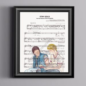Puede incluir: Una partitura musical de la canción "Stay Gold" del musical "The Outsiders". La música está escrita en notación estándar con la letra impresa debajo. La partitura presenta una ilustración de dos chicos sentados juntos, uno con cabello castaño y una chaqueta azul, el otro con cabello rubio y una camisa blanca.
