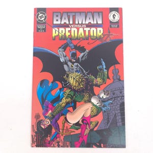May include: A comic book cover for "Batman Versus Predator" issue 4 of 4. The cover features Batman battling the Predator, with a woman in a purple and blue costume. The background is red with the title text in white and yellow.