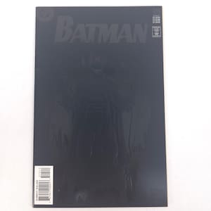 May include: A Batman comic book with a dark cover featuring the Batman logo and a shadowy figure of Batman. The comic has a glossy finish and a barcode on the bottom left corner.