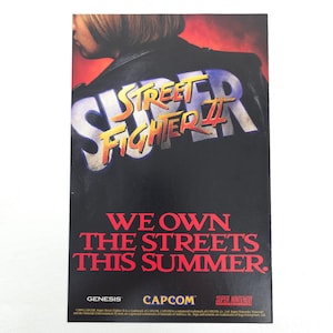 May include: A promotional poster for Street Fighter II, featuring the game's logo in yellow and blue on a black background. The text "WE OWN THE STREETS THIS SUMMER" is displayed in red. Logos for Genesis, Capcom, and Super Nintendo are also present.