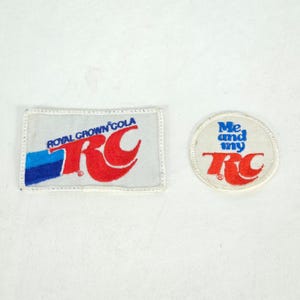 May include: Two vintage RC Cola patches. One rectangular patch features the words "Royal Crown Cola" and the RC logo in red, blue, and white. The other is a circular patch with the words "Me and my RC" and the RC logo.